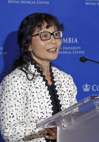A woman with glasses speaks at a podium